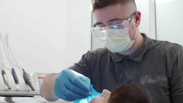 Male dentist cleaning root canal and cauterizing dental nerve in the modern dental clinic. Oral surgeon treats carefully patient teeth. Professional endodontist treating root canals. Endodontics.