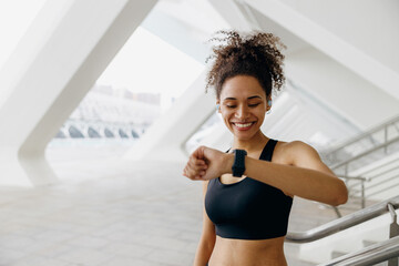 Smiling woman in sportswear looking on smartwatch after running. Outdoor sports in the morning