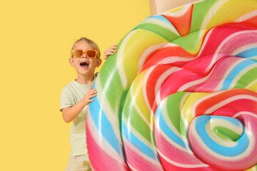 Cute little boy with candy shaped swim mattress on yellow background