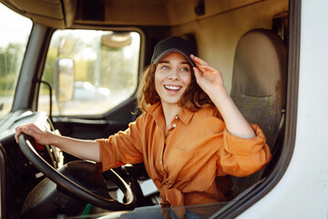 Portrait of young woman professional driver sitting and driving a big truck. Inside of vehicle. Female trucker. People and industrial transportation concept. - obrazy, fototapety, plakaty