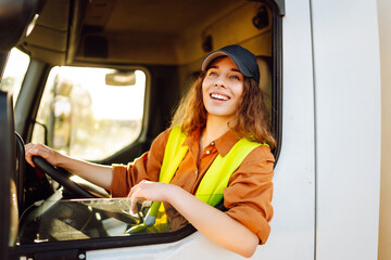 Portrait of young woman professional driver sitting and driving a big truck. Inside of vehicle....