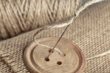 burlap, wooden button and sewing needle close up