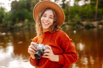 Woman in hat and warm autumn clothes with a mirror film camera posing on a nature.Travel blog....