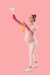 Young pregnant woman with squeegee and detergent on pink background