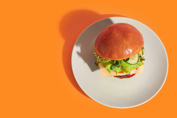 Plate with tasty burger on orange background