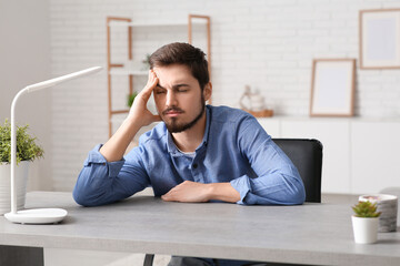 Tired young businessman at table in office - obrazy, fototapety, plakaty