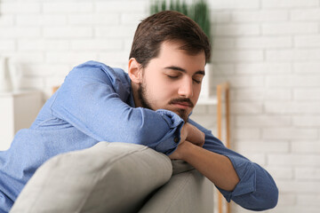 Tired young man sitting on couch at home, closeup - obrazy, fototapety, plakaty