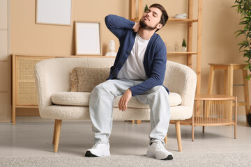 Tired young man sitting on sofa at home - obrazy, fototapety, plakaty
