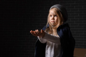 Homeless little girl begging for money near grey brick wall