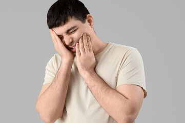 Young man suffering from toothache on light background