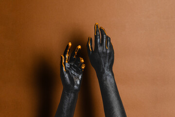 Elegant woman's hands with black and gold painted on her skin on brown background. High Fashion art concept