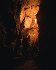 Exploradores en una cueva con una antorcha  - obrazy, fototapety, plakaty
