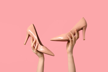 Female hands with stylish beige high heels on pink background
