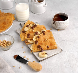 Crepes (thin pancakes) with banana slices, chocolate and pine nuts on ceramic board. Homemade...