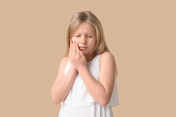 Young girl suffering from toothache on beige background