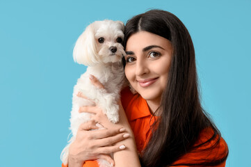Young happy woman holding her cute Bolognese dog on blue background