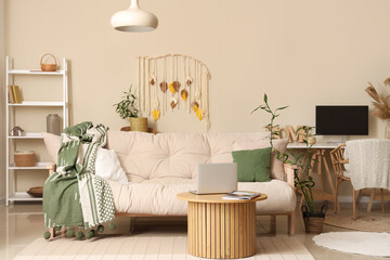 Comfortable sofa with plaid, coffee table with laptop and bamboo plant in living room