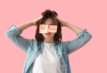 Beautiful young stressed woman with sticky notes with text I'M TIRED on pink background. Stress Awareness Month - obrazy, fototapety, plakaty