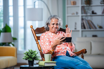 3. mid age Indian asian man with grey hair using smartphone while sitting on rocking chair at home