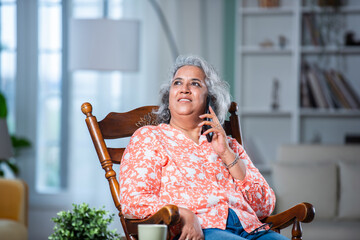 3. mid age Indian asian man with grey hair using smartphone while sitting on rocking chair at home