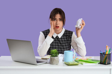 Young stressed businesswoman with laptop trying to meet deadline at table on purple background. Stress Awareness Month - obrazy, fototapety, plakaty