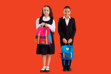 Happy little pupils with backpacks on red background