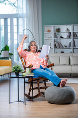 Indian mid age lady with grey hair checking financial documents at home while sitting on rocking...