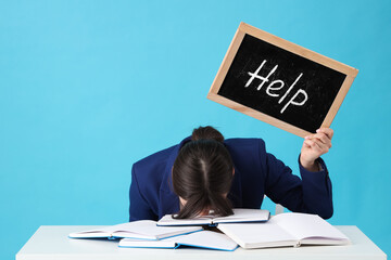Young stressed businesswoman holding chalkboard with word HELP on blue background. Stress Awareness Month - obrazy, fototapety, plakaty