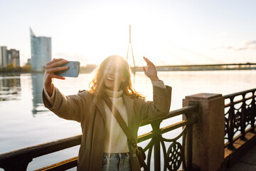 Selfie time. Young woman holding mobile phone taking selfie photo using smartphone camera standing...