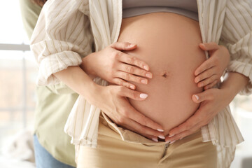 Young pregnant woman with her wife touching belly at home, closeup