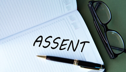 ASSENT - word in notebook on green background with glasses and pen