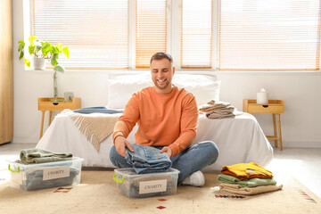 Young man folding charity clothes in bedroom