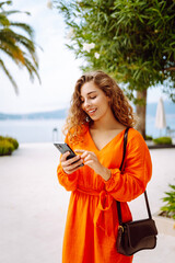 Young woman walking down the street and using mobile phone.  Travel, fashion, communication, blogging concept. 