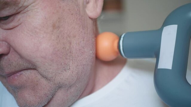 Massage percussion gun at work. Senior man massaging his neck, close-up.