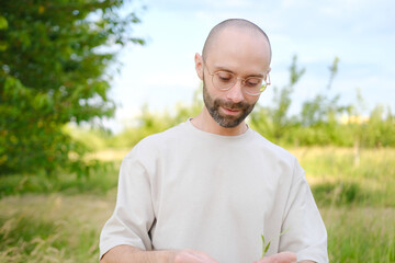 young charismatic man holds young green leaf in hand, caring for nature, green garden in background, concept ecological balance, joy of connecting with nature