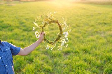 happy boy holding wreath in hand, floral crown on green sunlit meadow, seen from behind, beauty...