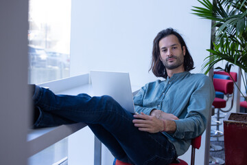 portrait d'un homme qui travaille dans un espace ouvert de co working. il est détendu et travaille avec un ordinateur portable sur ses genoux