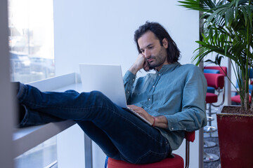 portrait d'un homme qui travaille dans un espace ouvert de co working. il est détendu et travaille avec un ordinateur portable sur ses genoux - 781598180