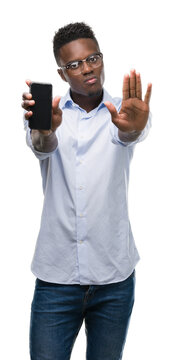 Young african american man using smartphone with open hand doing stop sign with serious and confident expression, defense gesture