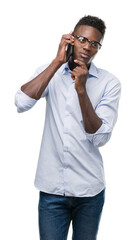 Young african american man using smartphone serious face thinking about question, very confused idea