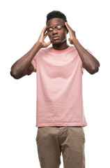 Young african american man wearing pink t-shirt with hand on head for pain in head because stress. Suffering migraine.