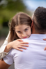 Young girl tightly embraces her father, looking into the camera.