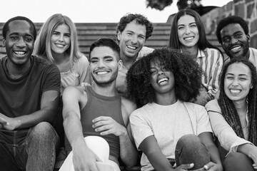 Group of multiracial friends sitting on stairs in the city while smiling on camera - Diverse young...