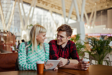 An urban couple with tablet sitting at cafe, chatting and drinking coffee