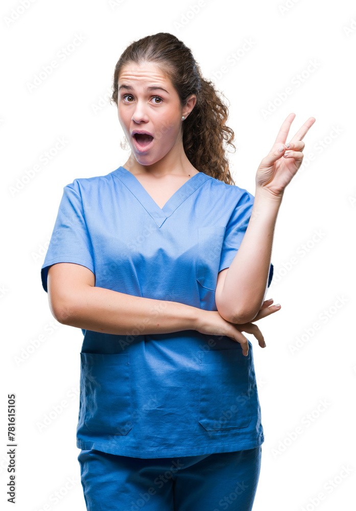 Wall mural Young brunette doctor girl wearing nurse or surgeon uniform over isolated background smiling with happy face winking at the camera doing victory sign. Number two.