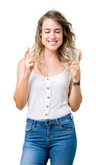 Young beautiful blonde woman over isolated background smiling crossing fingers with hope and eyes closed. Luck and superstitious concept.