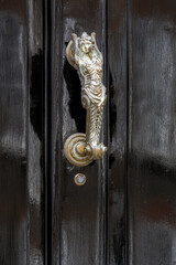 Metal door knocker on a black wooden door in the shape of a mermaid
