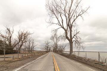 A lonely isolated road straddling the shores of Lake Erie in Long Point, Ontario. Weathered pavement.  - obrazy, fototapety, plakaty