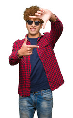 Young handsome man with afro hair wearing sunglasses smiling making frame with hands and fingers with happy face. Creativity and photography concept.