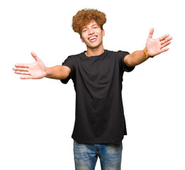 Young handsome man with afro hair wearing black t-shirt looking at the camera smiling with open...